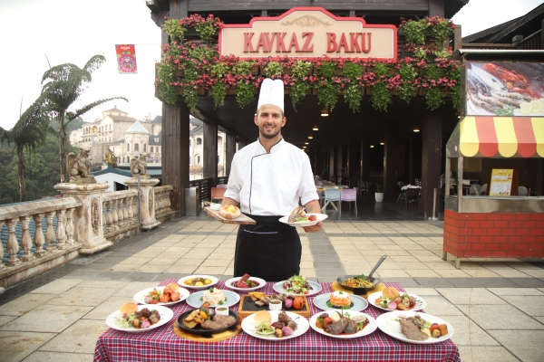 Chef présentant une variété de plats gastronomiques au restaurant Kavkaz Baku, dans un cadre extérieur pittoresque avec une architecture traditionnelle.