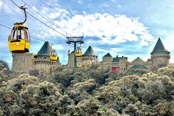 Des téléphériques baptisés "Ba Na Hills" survolent un château de conte de fées doté de multiples tourelles, niché au milieu d'une végétation dense sous un ciel partiellement nuageux.